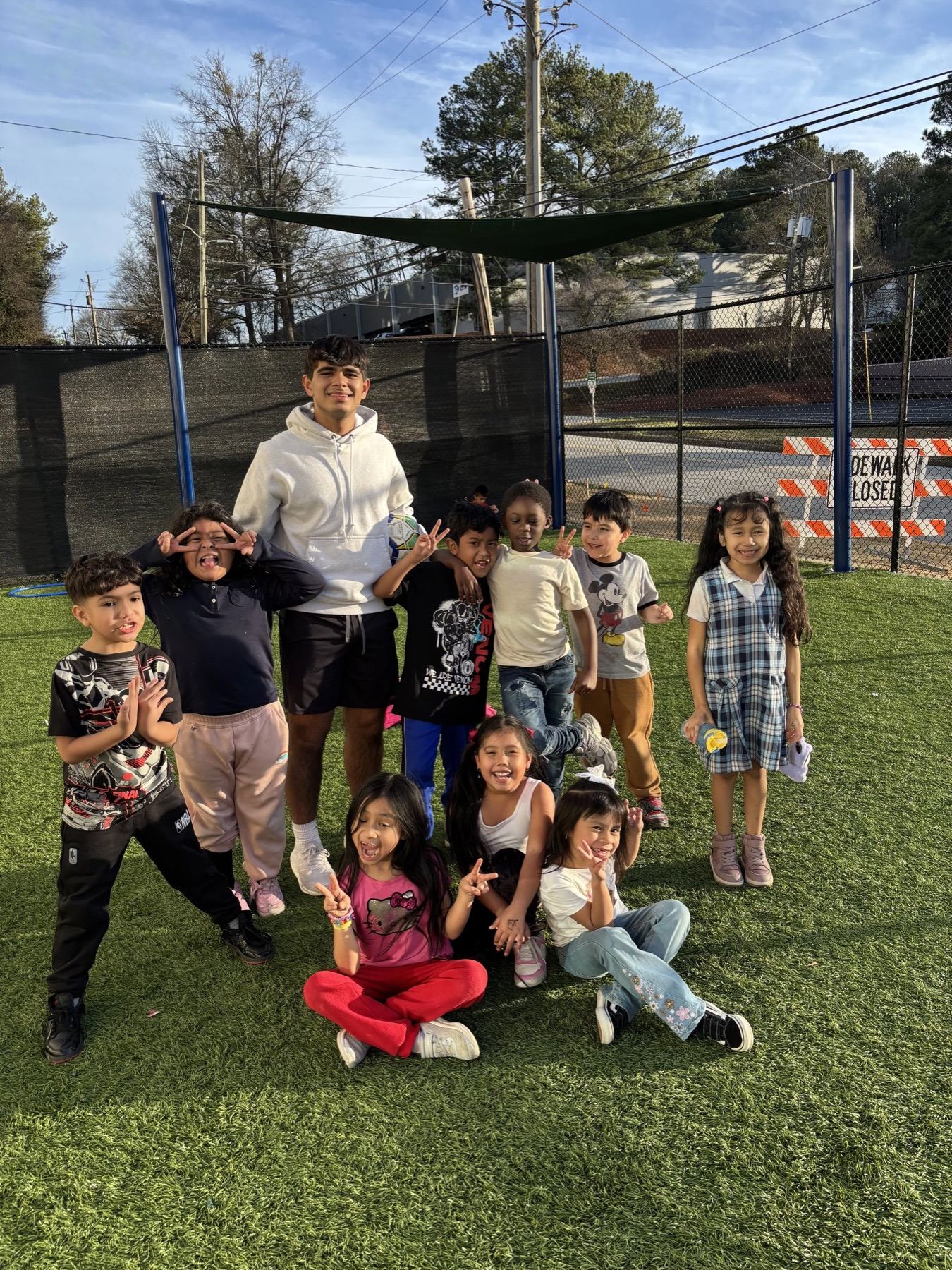 A group of children smiling together on the grass in front of a trampoline net