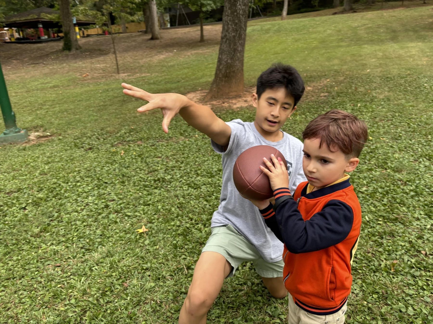 Two boys grinning as they play catch with a football on a grass field
