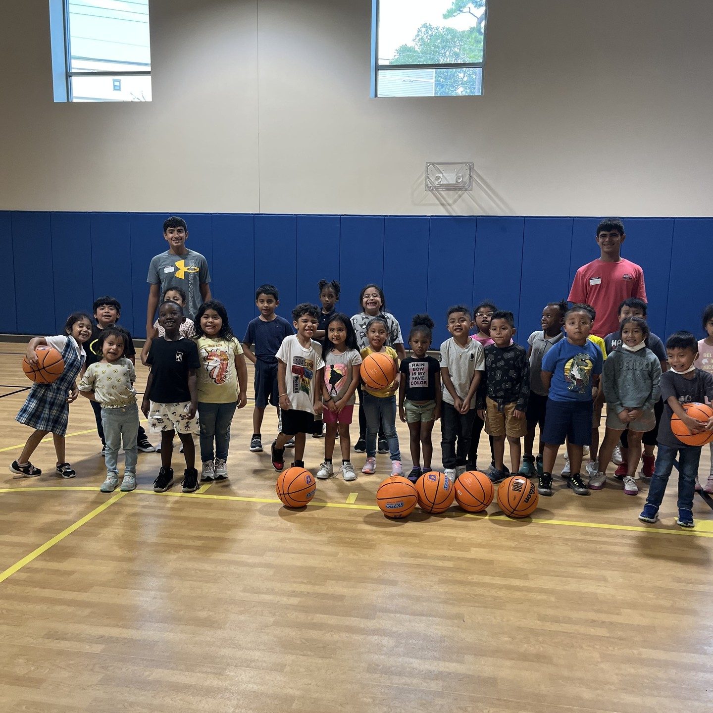 Children lined up on a gym floor each holding a basketball after a session at Agape