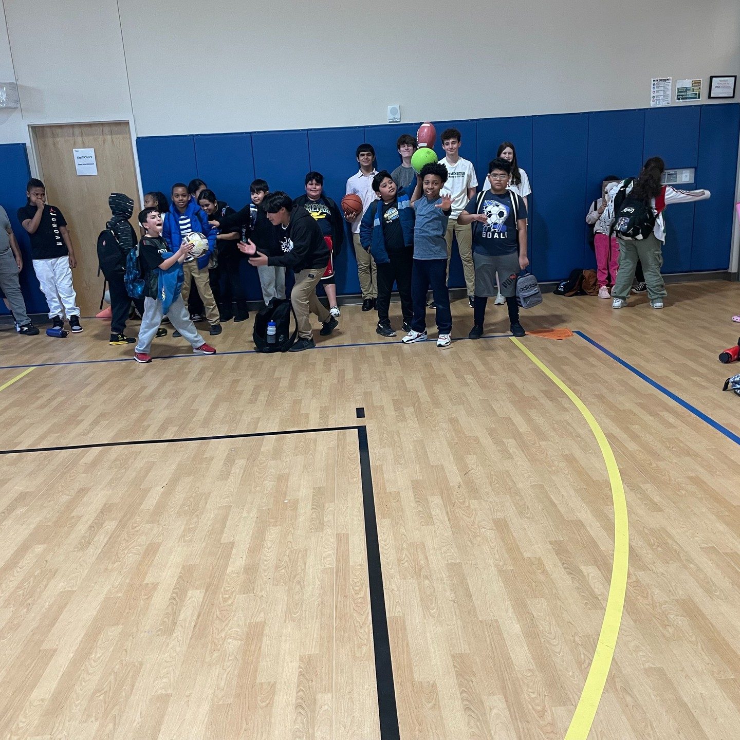 A large group of children gathered on a gymnasium floor beneath the basketball hoop