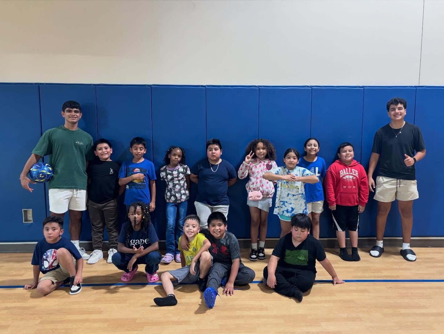 A big group of children and teen volunteers posing together on a gymnasium floor after a fall session