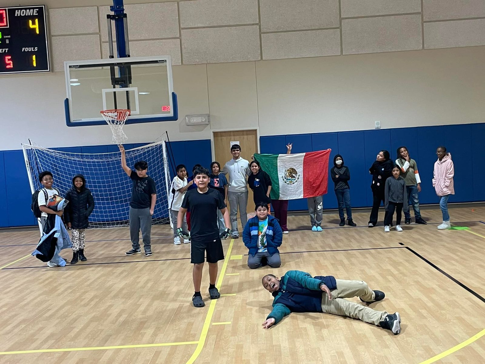 Children celebrating in a gym after a game, one holding up a Mexican flag