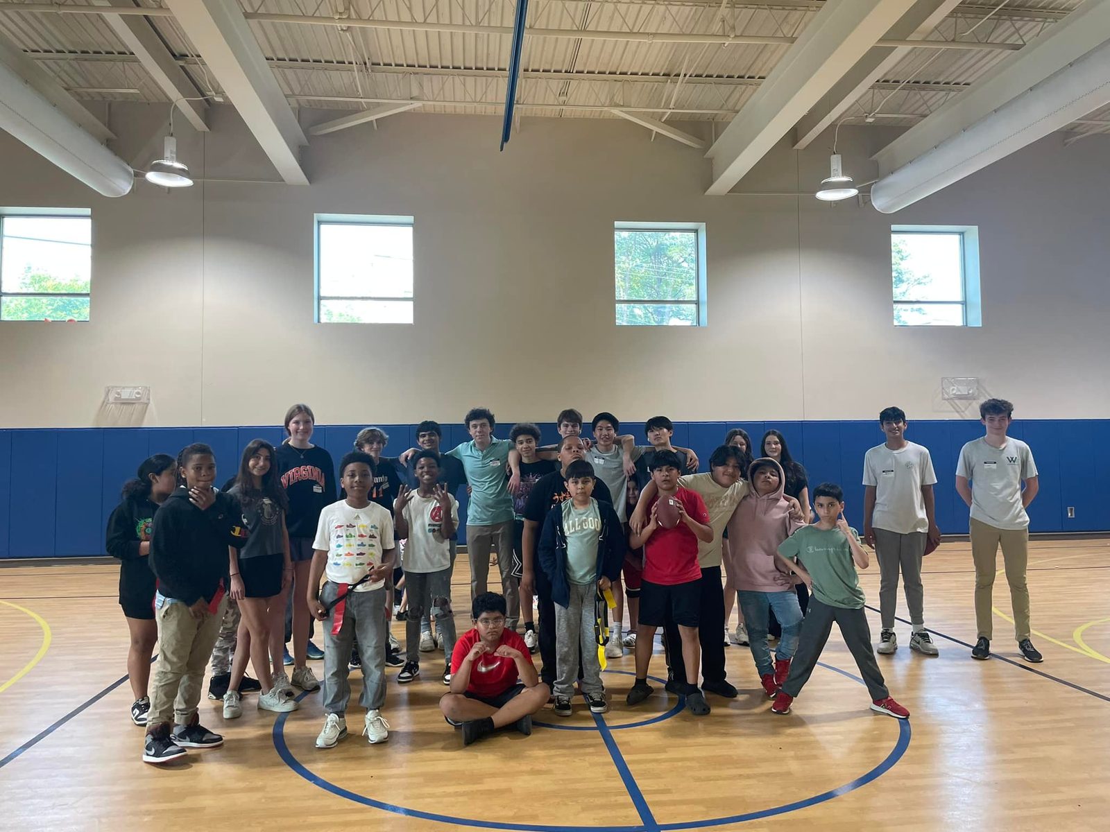 A large group of children and teen volunteers on a gymnasium floor after flag football