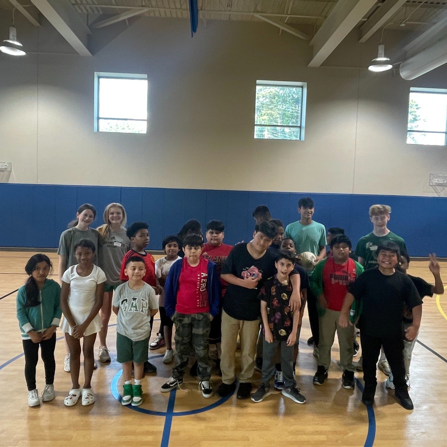 Children and volunteers posing together on a gym floor after a game of soccer