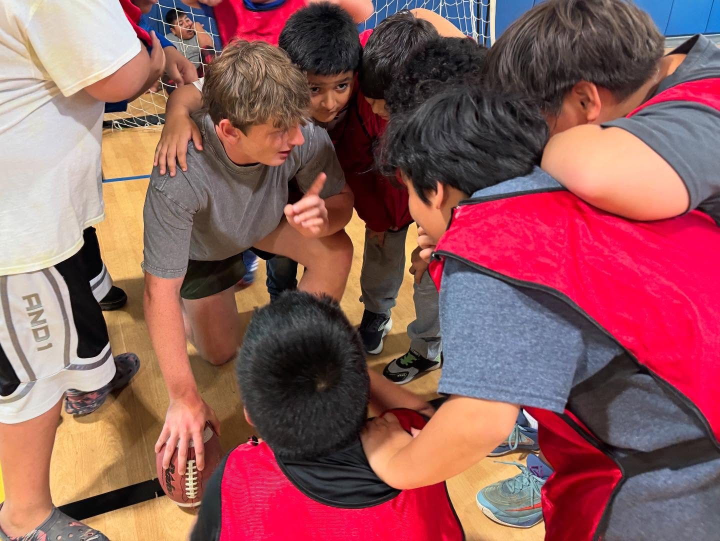 Children in a tight huddle with their arms around each other during summer programming