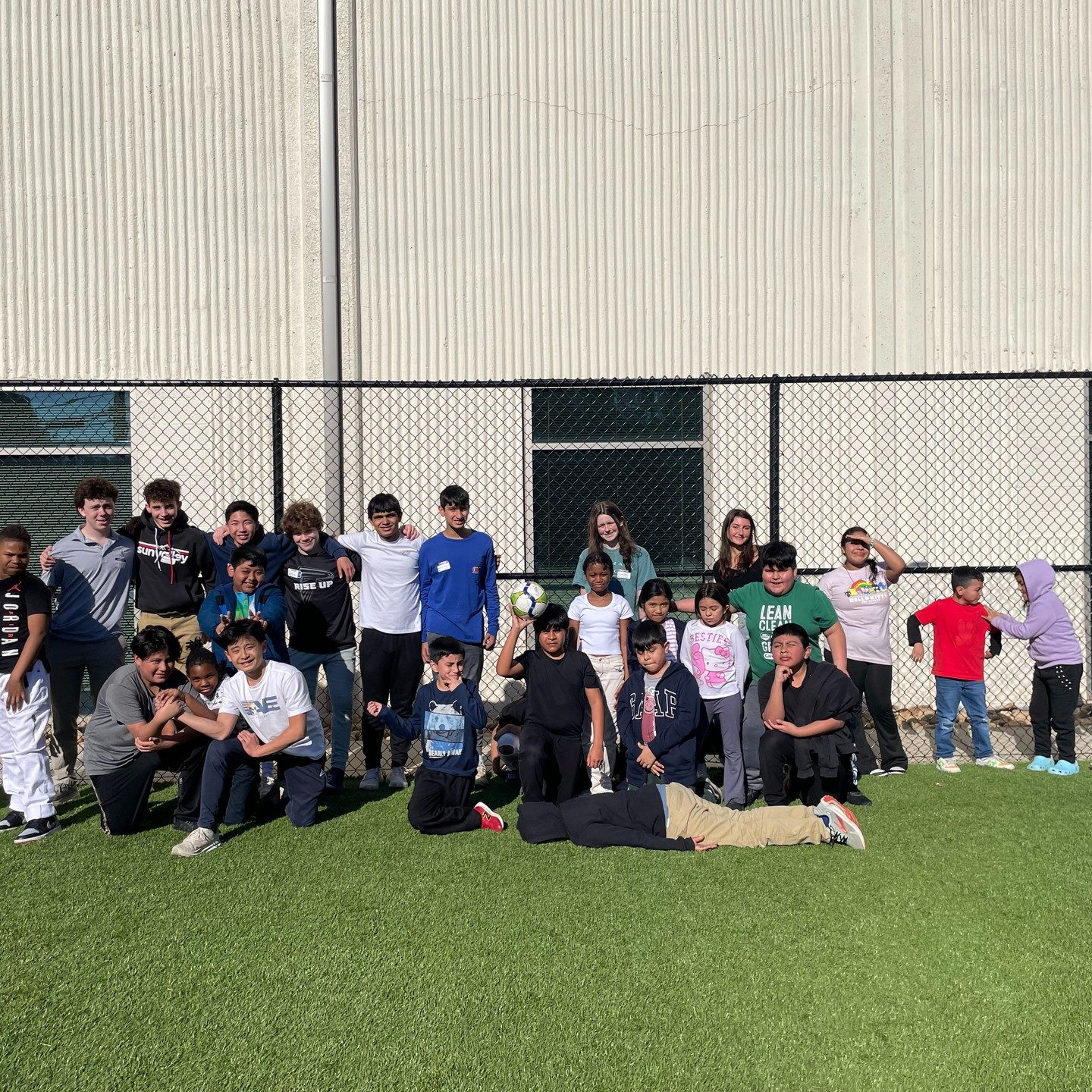 Children and volunteers sitting and standing together on a turf field after a soccer game
