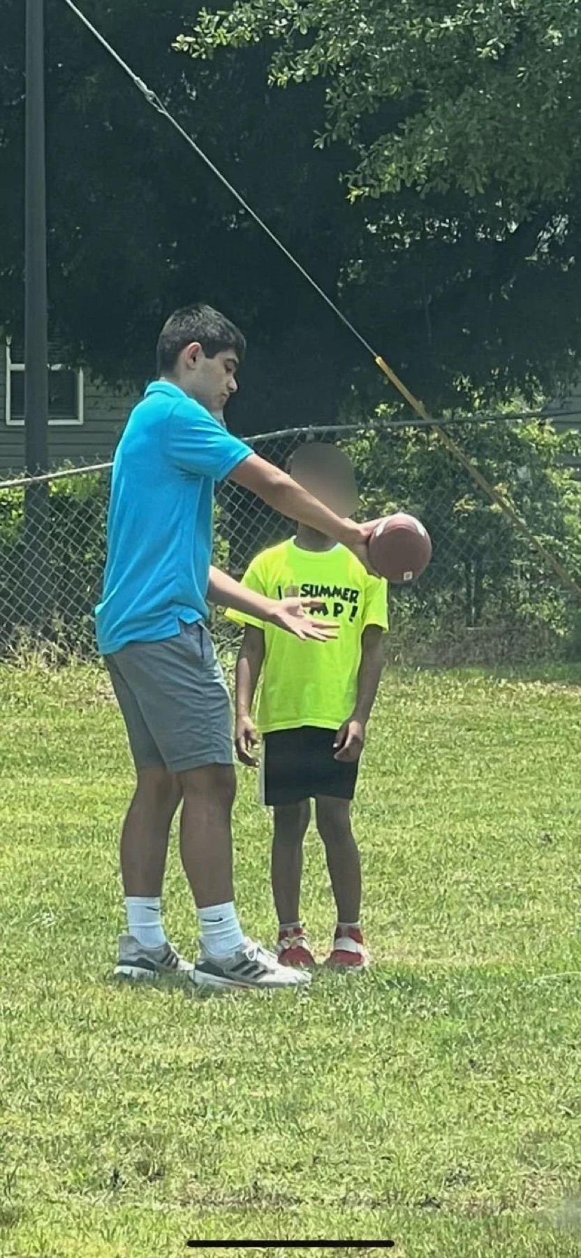 A volunteer in a bright shirt showing a child how to hold a basketball