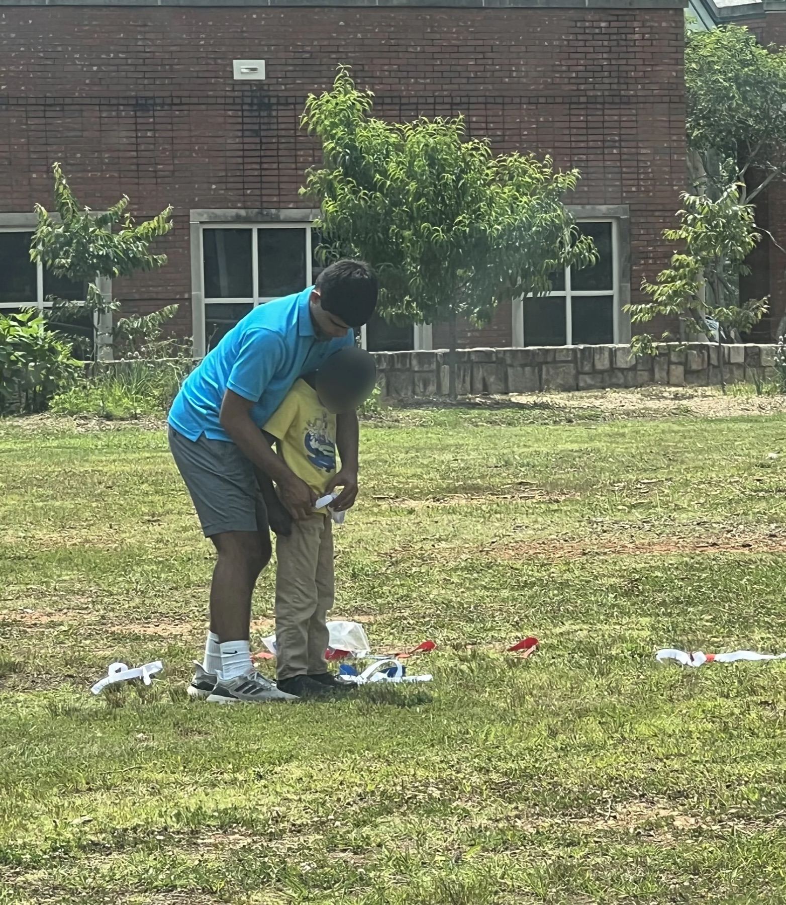 A volunteer crouching beside a child on the field to demonstrate a technique