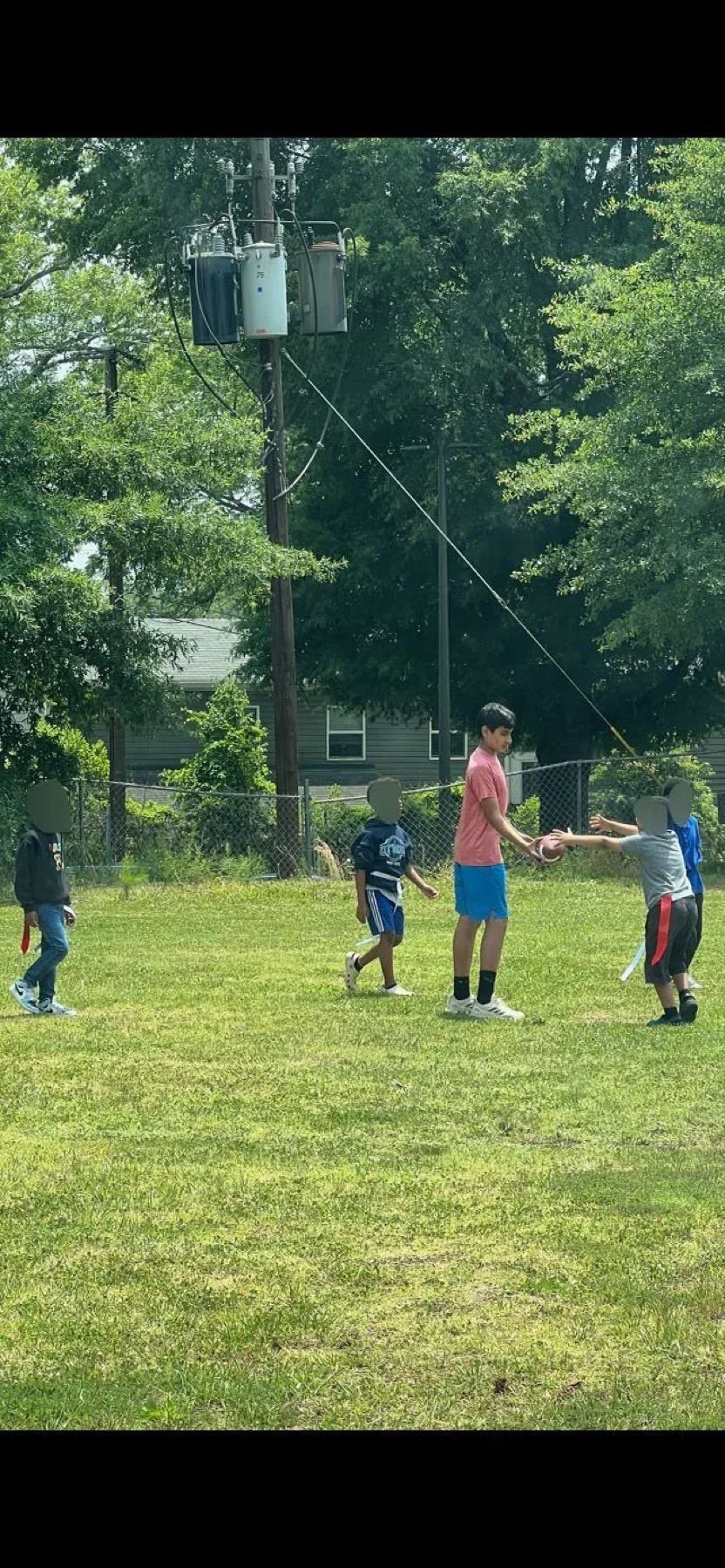 Children playing on a grass field beside a chain-link fence