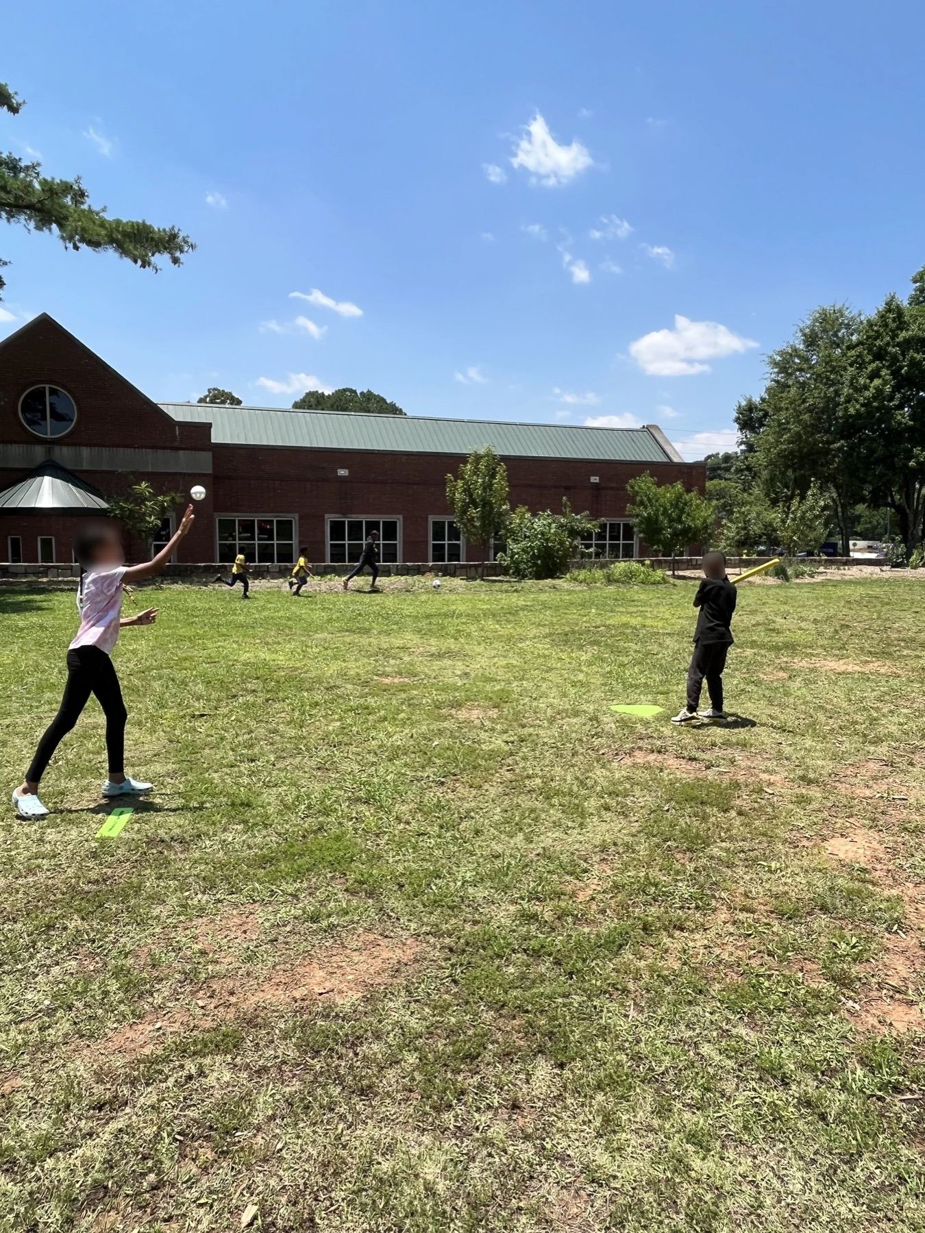 Children playing on a grass field in front of a brick community center building