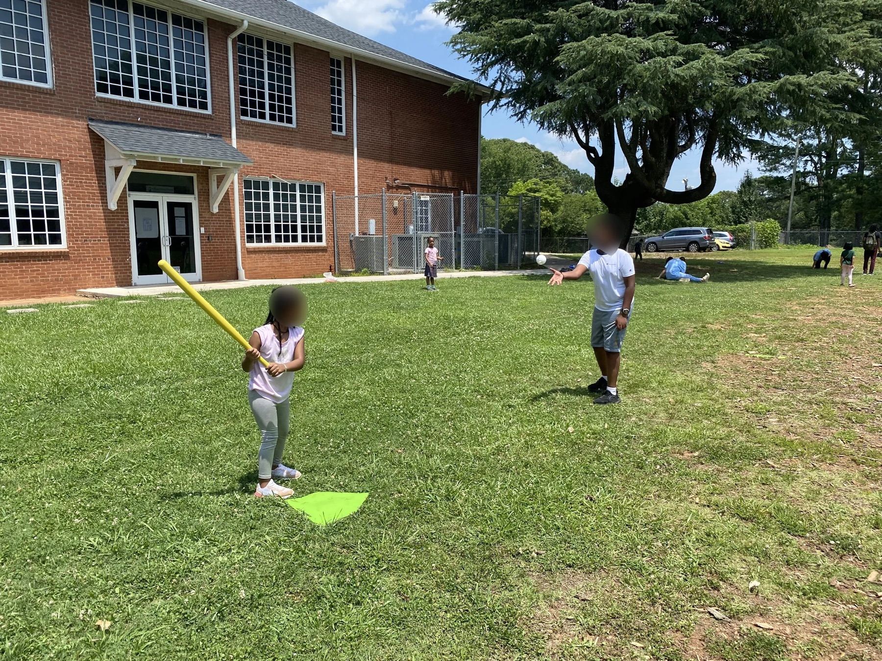 A child swinging a bat on a grass field beside a brick building