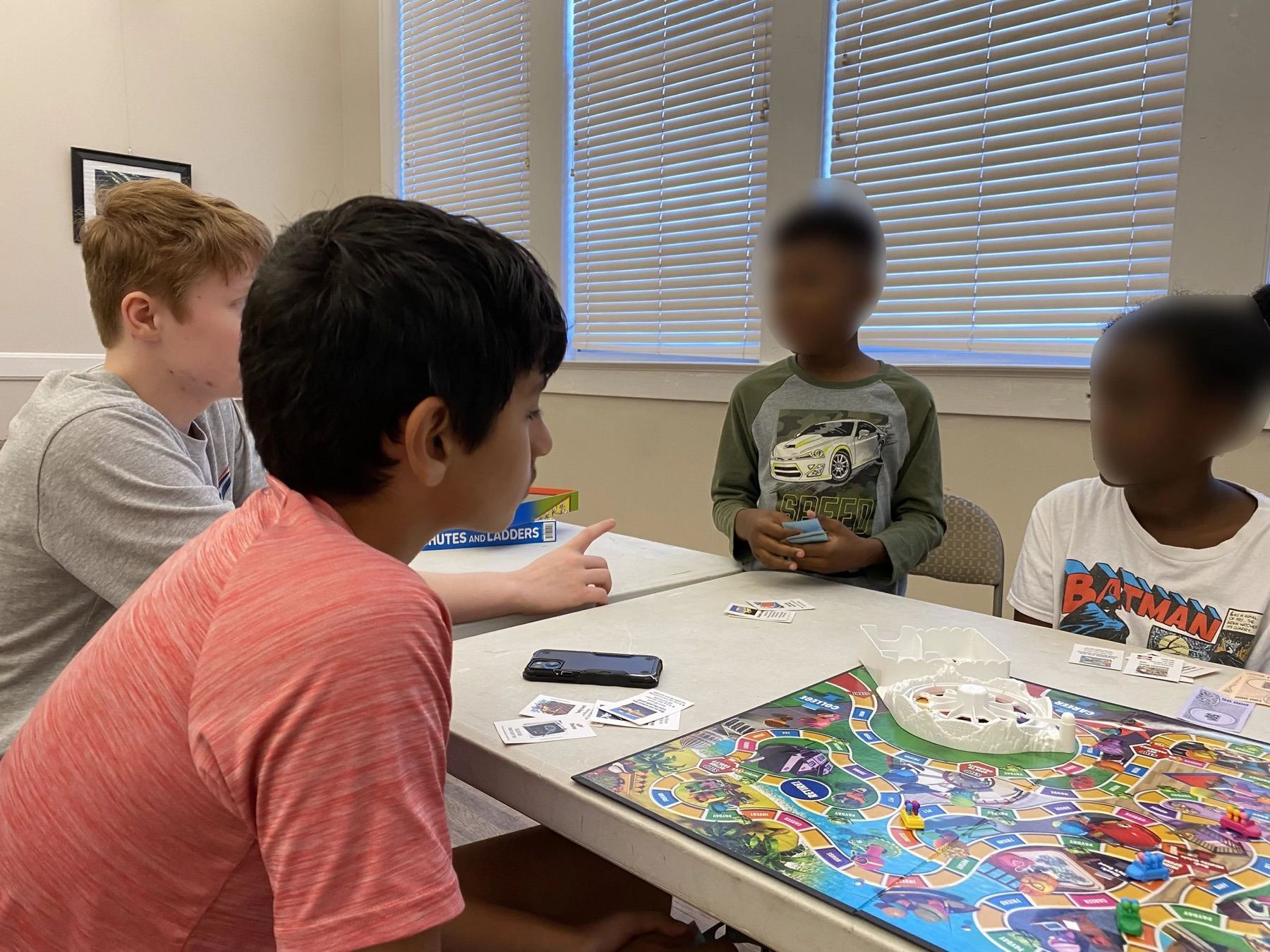 Children and volunteers sitting around a table playing board games together inside a community center