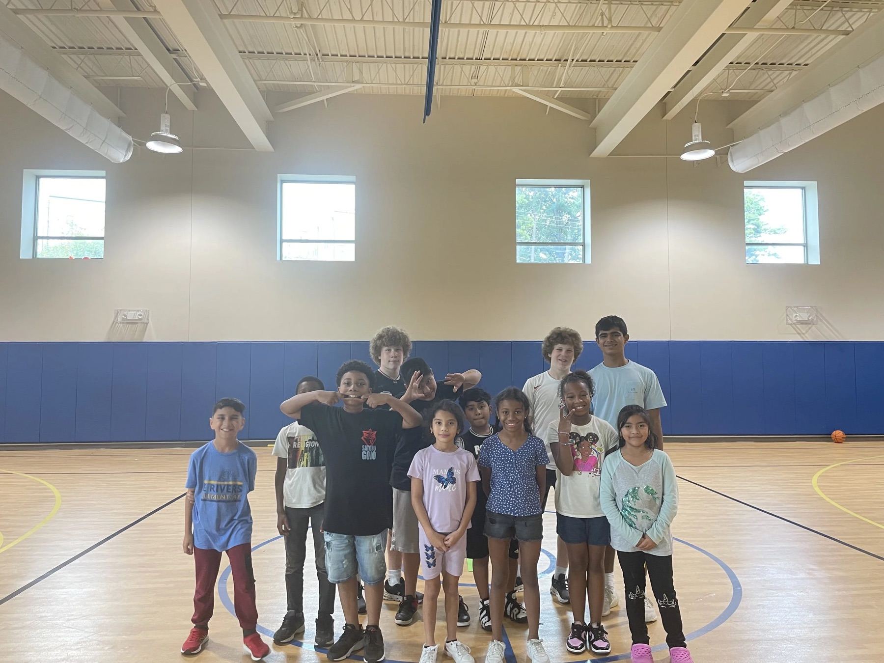 Children lined up shoulder to shoulder across a gymnasium floor smiling at the camera