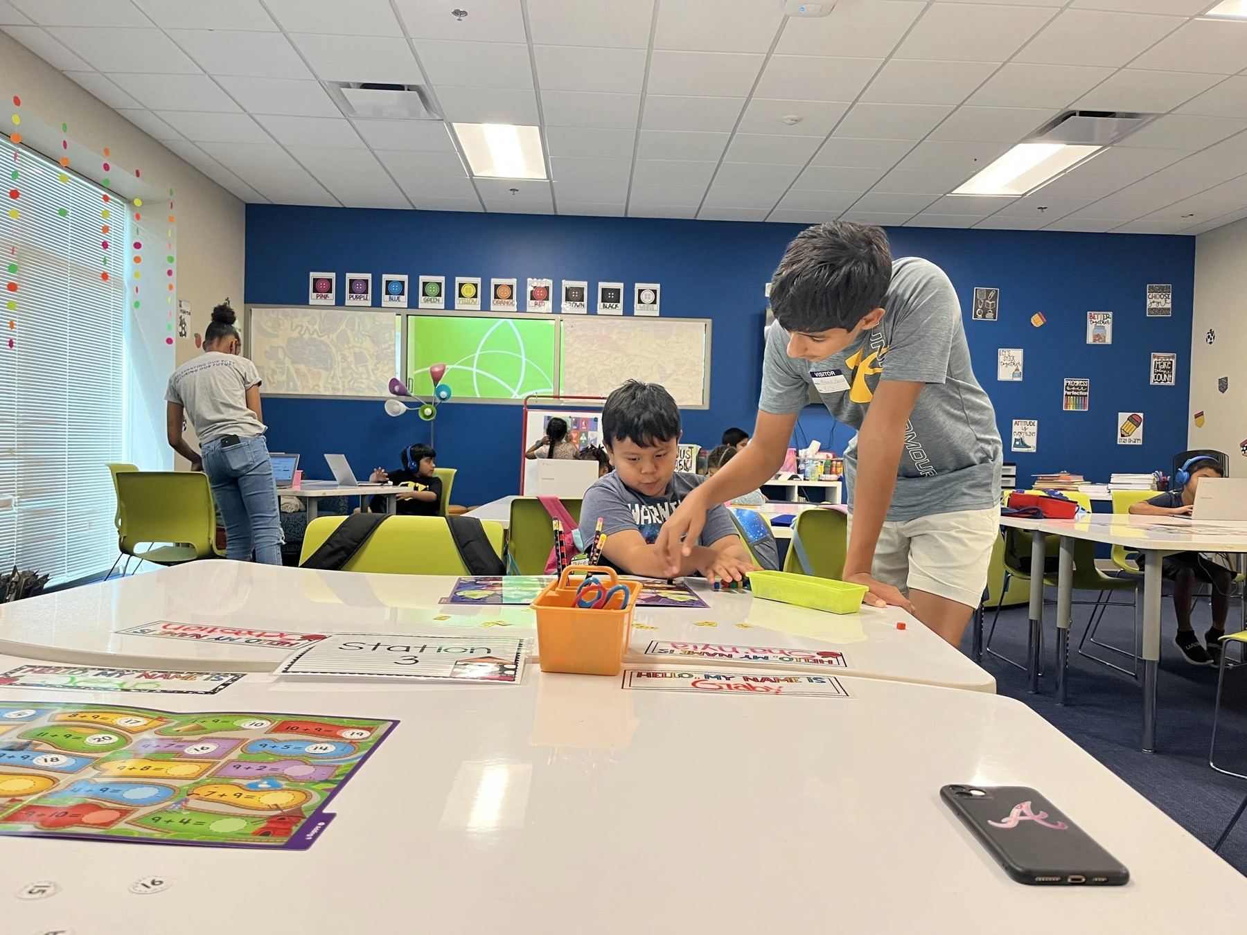 A volunteer helping children with board games spread across a classroom table