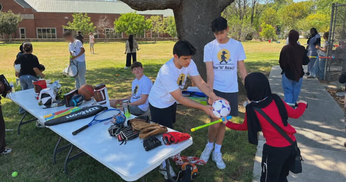 Still from the WSB-TV segment: Rise 'N' Reach volunteers in team shirts handing out sports equipment to children at an outdoor table
