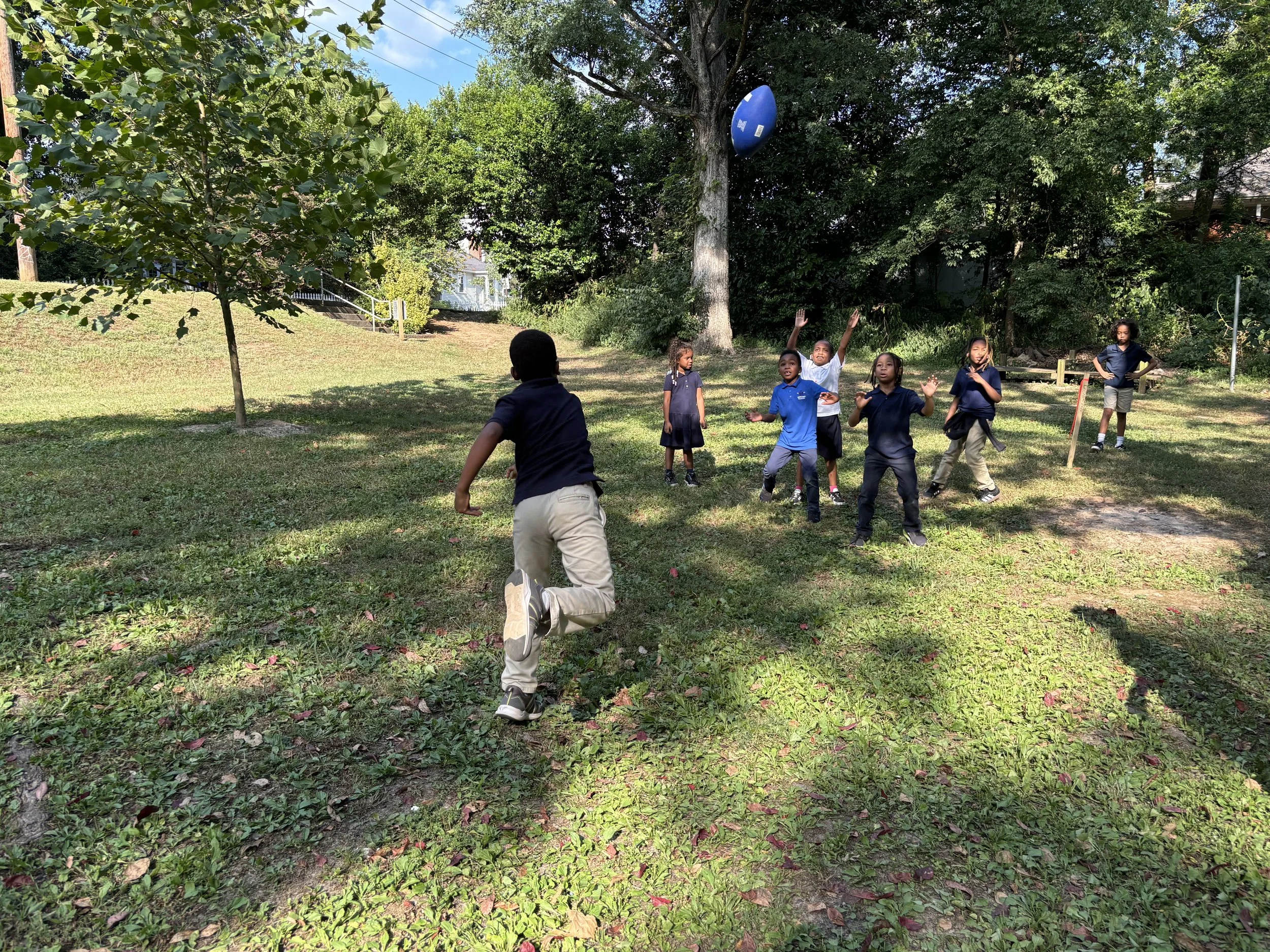Children running across a sunlit grass field during a Rise 'N' Reach session